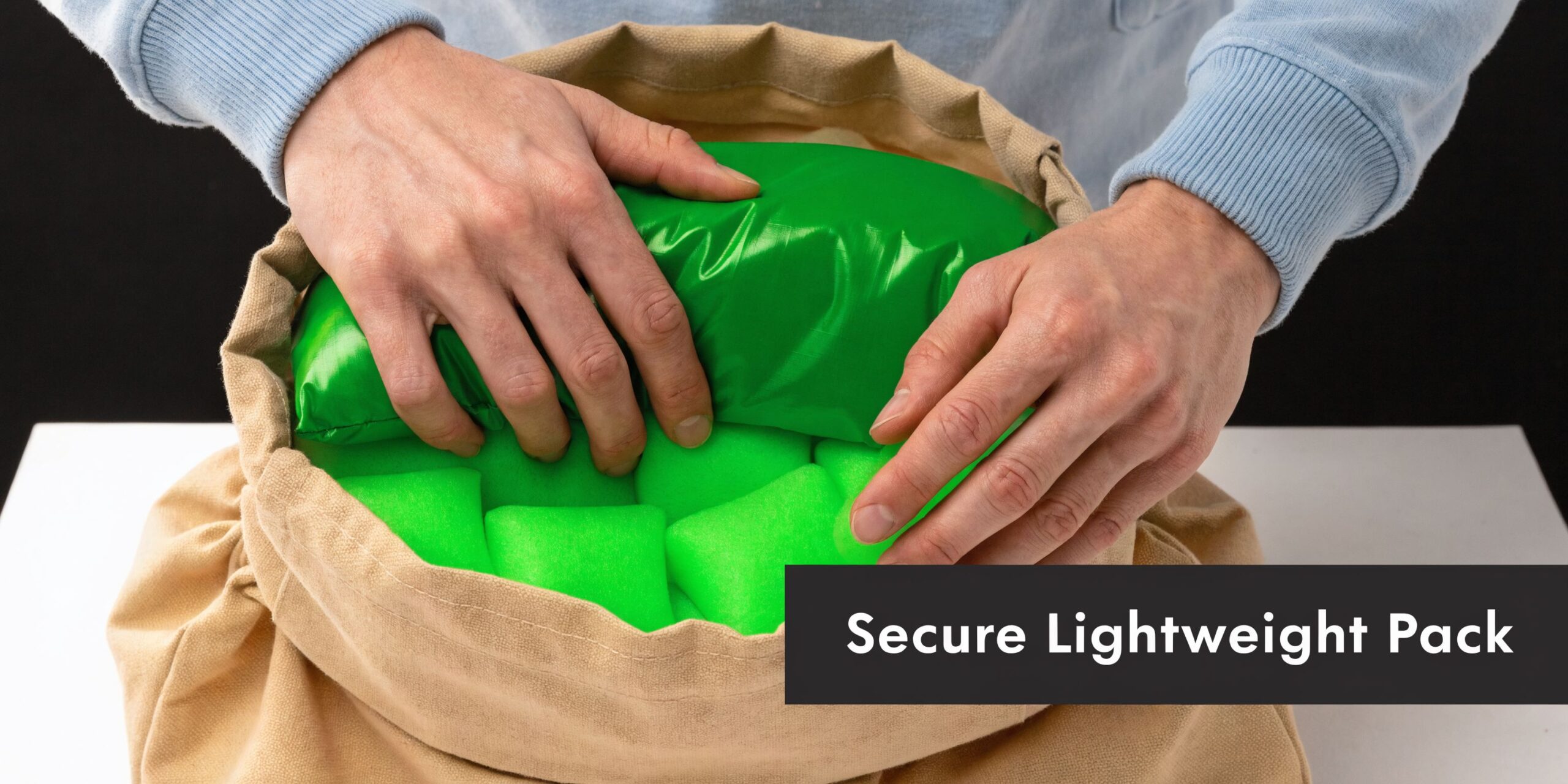A person securely packing bright green foam cushioning blocks into a beige canvas mailing satchel bag.